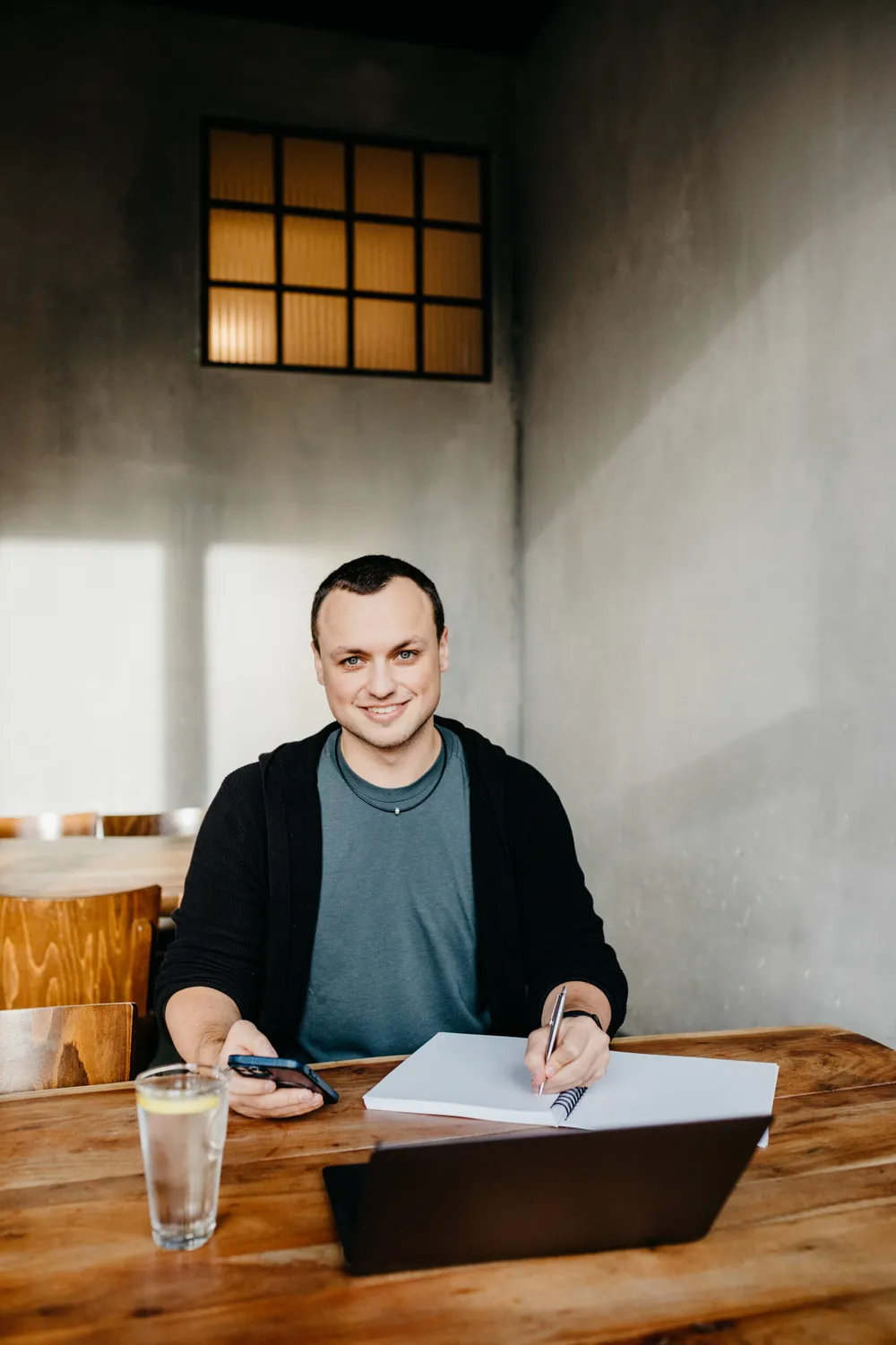 Timo Maletschek am Schreibtisch mit Laptop, Notizbuch und Wasserglas